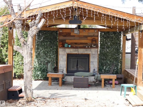 Covered patio featuring a stone-clad fireplace with wood-finish mantel, wood-plank accent wall, and decorative privacy screens - 5220 - 56 Street, Barrhead, AB - Outdoor With Fireplace
