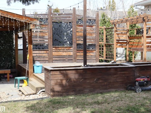 Multi-level wood decking with integrated planters, a covered patio area, privacy screens with decorative metal inserts, and an adjacent wood pergola - 5220 - 56 Street, Barrhead, AB - Outdoor