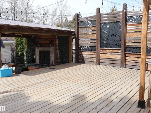 Expansive outdoor wood-finish deck with a covered lounge area featuring a stone fireplace and wood-plank accent wall - 5220 - 56 Street, Barrhead, AB - Outdoor