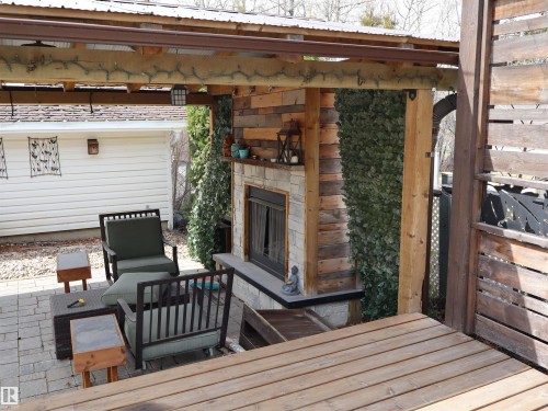 Covered patio featuring a stone-faced fireplace with a dark mantel, wood-plank accent walls, a durable metal roof, and a paver stone patio surface - 5220 - 56 Street, Barrhead, AB - Outdoor With Exterior