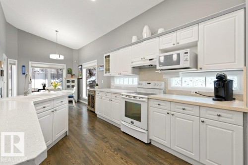 Kitchen with white appliances, white cabinetry, hanging light fixtures, dark wood-style flooring, and lofted ceiling - 8 Osborne Close, St. Albert, AB - Indoor Photo Showing Kitchen