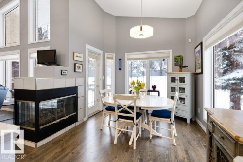 Dining room with a high ceiling, dark wood-style flooring, and a tile fireplace - 8 Osborne Close, St. Albert, AB - Indoor Photo Showing Dining Room With Fireplace