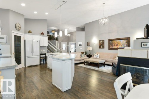 Kitchen featuring a high ceiling, freestanding refrigerator, white cabinetry, a kitchen island with sink, and dark wood-style floors - 8 Osborne Close, St. Albert, AB - Indoor
