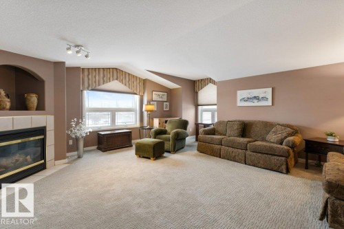 Carpeted living room with a tiled fireplace, a textured ceiling, and track lighting - 8 Osborne Close, St. Albert, AB - Indoor Photo Showing Living Room With Fireplace
