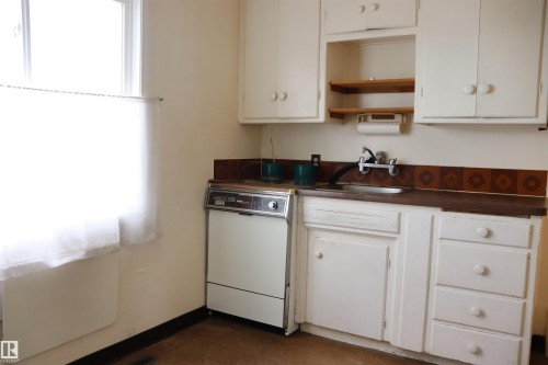 Kitchen with dark countertops, white dishwasher, open shelves, and white cabinets - 11250 72 Avenue, Edmonton, AB - Indoor Photo Showing Kitchen