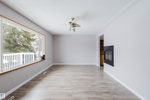 Empty room featuring light wood finished floors, ceiling fan, a glass covered fireplace, and a textured ceiling - 6048 105B Street Nw, Edmonton, AB - Indoor Photo Showing Other Room