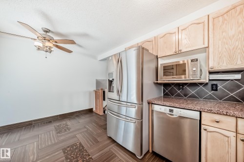 Kitchen with stainless steel appliances, light wood finish cabinets, ceiling fan, decorative backsplash, and a textured ceiling - 7011 190B Street, Edmonton, AB - Indoor Photo Showing Kitchen