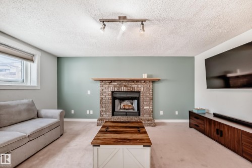 Living area featuring light carpet, a brick fireplace, a textured ceiling, and rail lighting - 7011 190B Street, Edmonton, AB - Indoor Photo Showing Living Room With Fireplace
