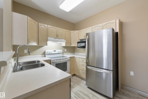 Kitchen with light wood finish cabinets, freestanding refrigerator, electric stove, light countertops, and a textured ceiling - 232 15499 Castle Downs Road, Edmonton, AB - Indoor Photo Showing Kitchen With Double Sink