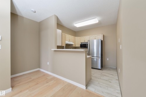 Kitchen with freestanding refrigerator, light wood-type flooring, light countertops, a peninsula, and a textured ceiling - 232 15499 Castle Downs Road, Edmonton, AB - Indoor Photo Showing Other Room