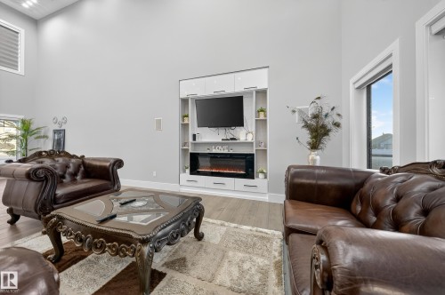 Living room with light wood-style flooring, a high ceiling, a glass covered fireplace, and built in shelves - 4406 Triomphe Close, Beaumont, AB - Indoor Photo Showing Living Room