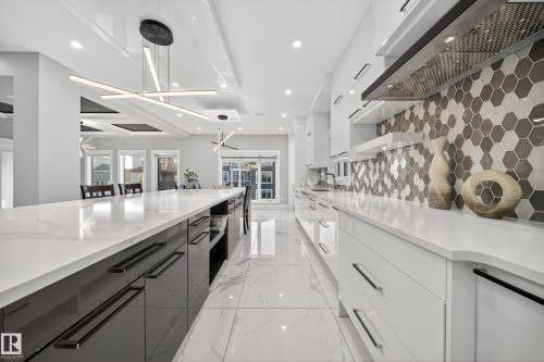 Kitchen with modern cabinets, two tone cabinetry, ventilation hood, light stone countertops, and pendant lighting - 4406 Triomphe Close, Beaumont, AB - Indoor