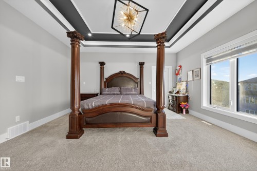 Bedroom with a tray ceiling, light colored carpet, ornate columns, and suspended lighting - 4406 Triomphe Close, Beaumont, AB - Indoor Photo Showing Bedroom