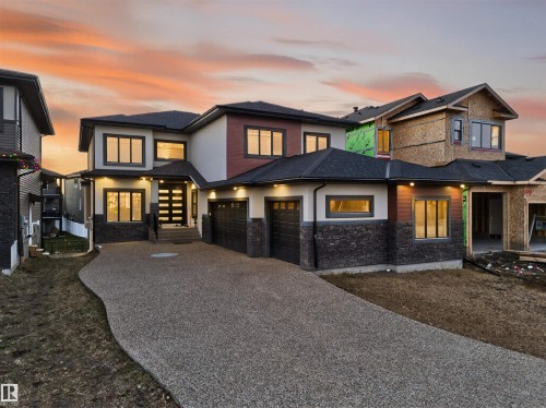 View of front of house with gravel driveway, stone siding, stucco siding, and roof with shingles - 4406 Triomphe Close, Beaumont, AB - Outdoor With Facade