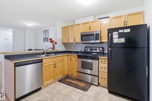 Kitchen with stainless steel appliances, tasteful backsplash, a peninsula, light flooring, and light wood finish cabinets - 407 2305 35A Avenue, Edmonton, AB - Indoor Photo Showing Kitchen With Double Sink