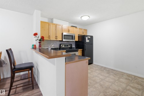 Kitchen featuring a peninsula, dark countertops, stainless steel appliances, a kitchen breakfast bar, and light wood finish cabinetry - 407 2305 35A Avenue, Edmonton, AB - Indoor Photo Showing Kitchen With Double Sink