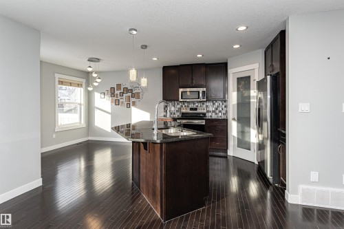 Kitchen featuring dark wood finish cabinetry, stainless steel appliances, pendant lighting, dark stone counters, and backsplash - 6963 19A Avenue, Edmonton, AB - Indoor Photo Showing Kitchen