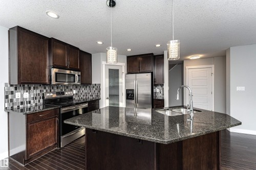 Kitchen featuring stainless steel appliances, dark stone counters, dark wood finish cabinetry, dark wood finished floors, and hanging light fixtures - 6963 19A Avenue, Edmonton, AB - Indoor Photo Showing Kitchen With Double Sink With Upgraded Kitchen