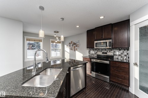 Kitchen featuring stainless steel appliances, pendant lighting, dark stone counters, tasteful backsplash, and dark wood finish cabinetry - 6963 19A Avenue, Edmonton, AB - Indoor Photo Showing Kitchen With Double Sink With Upgraded Kitchen