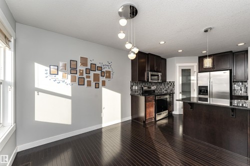 Kitchen featuring hanging light fixtures, stainless steel appliances, dark wood finish cabinetry, a breakfast bar area, and dark stone counters - 6963 19A Avenue, Edmonton, AB - Indoor Photo Showing Kitchen