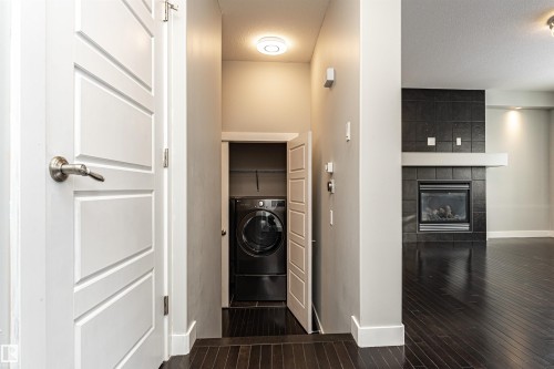 Laundry area with washer / dryer, dark wood-style flooring, a tiled fireplace, and a textured ceiling - 6963 19A Avenue, Edmonton, AB - Indoor Photo Showing Other Room