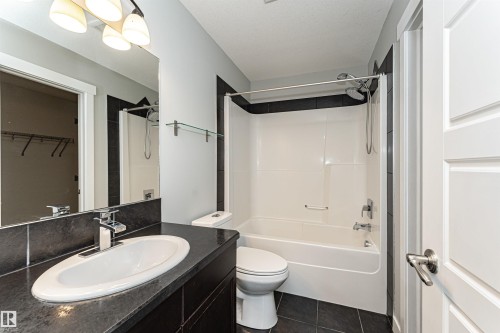 Full bath featuring shower / tub combination, vanity, a spacious closet, and dark tile patterned flooring - 6963 19A Avenue, Edmonton, AB - Indoor Photo Showing Bathroom