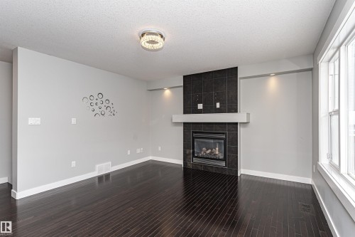Unfurnished living room featuring a fireplace, dark wood-style flooring, and a textured ceiling - 6963 19A Avenue, Edmonton, AB - Indoor With Fireplace