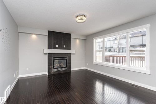 Unfurnished living room with a tile fireplace, dark wood finished floors, and a textured ceiling - 6963 19A Avenue, Edmonton, AB - Indoor With Fireplace