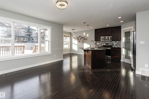 Kitchen with dark wood finish cabinetry, stainless steel appliances, backsplash, open floor plan, and a kitchen island with sink - 6963 19A Avenue, Edmonton, AB - Indoor Photo Showing Kitchen With Upgraded Kitchen
