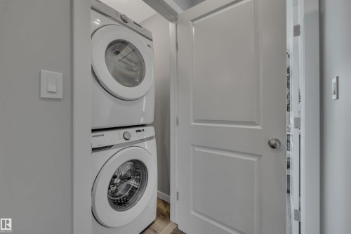 Laundry area featuring stacked washing machine and dryer and wood finished floors - 157 Larch Crescent, Leduc, AB - Indoor Photo Showing Laundry Room