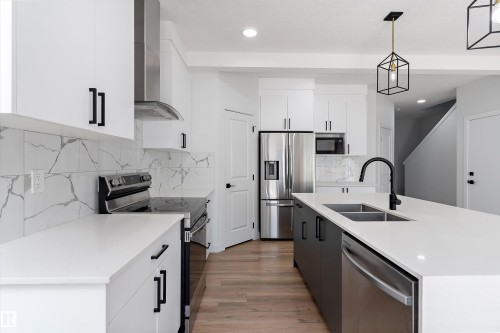 Kitchen with stainless steel appliances, pendant lighting, two tone color scheme, light stone countertops, and a kitchen island with sink - 5747 Kootook Way, Edmonton, AB - Indoor Photo Showing Kitchen With Double Sink With Upgraded Kitchen