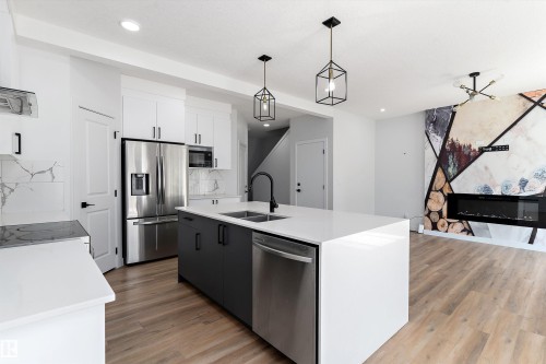 Two tone kitchen featuring stainless steel appliances, pendant lighting, a center island with sink, dual tone cabinets, and light stone counters - 5747 Kootook Way, Edmonton, AB - Indoor Photo Showing Kitchen With Double Sink With Upgraded Kitchen