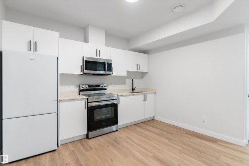 Kitchen featuring stainless steel appliances, white cabinets, light countertops, and light wood-type flooring - 5747 Kootook Way, Edmonton, AB - Indoor Photo Showing Kitchen