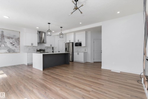 Two tone kitchen with an island with sink, pendant lighting, open floor plan, stainless steel appliances, and backsplash - 5747 Kootook Way, Edmonton, AB - Indoor Photo Showing Kitchen With Upgraded Kitchen