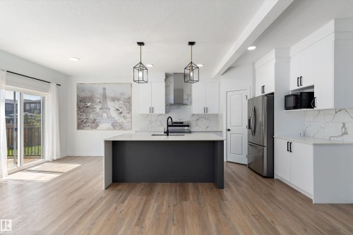 Kitchen with an island with sink, decorative light fixtures, tasteful backsplash, stainless steel appliances, and light stone counters - 5747 Kootook Way, Edmonton, AB - Indoor Photo Showing Kitchen With Upgraded Kitchen