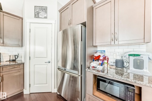 Kitchen with decorative backsplash, freestanding refrigerator, light stone countertops, black microwave, and dark wood-style flooring - 1908 69 Street, Edmonton, AB - Indoor Photo Showing Kitchen With Upgraded Kitchen