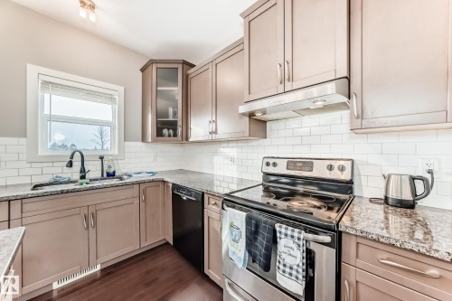 Kitchen featuring stainless steel electric range oven, light stone countertops, glass insert cabinets, dishwasher, and dark wood-style flooring - 1908 69 Street, Edmonton, AB - Indoor Photo Showing Kitchen With Upgraded Kitchen