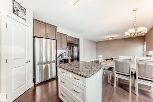 Kitchen with freestanding refrigerator, light stone countertops, a kitchen island, white cabinetry, and dark wood-style floors - 1908 69 Street, Edmonton, AB - Indoor Photo Showing Kitchen With Upgraded Kitchen