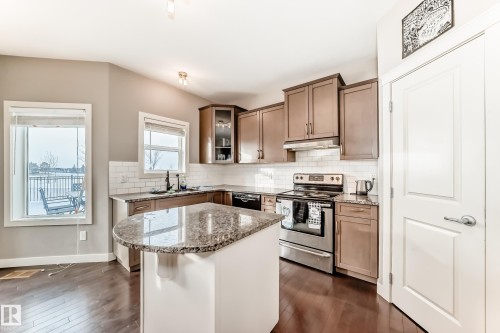 Kitchen with electric range, light stone counters, dark wood-style flooring, and glass fronted cabinets - 1908 69 Street, Edmonton, AB - Indoor Photo Showing Kitchen With Upgraded Kitchen