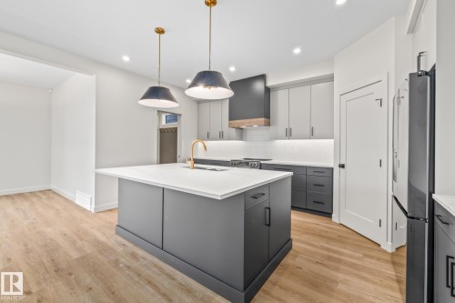Dual tone kitchen featuring two tone color scheme, pendant lighting, a center island with sink, light wood-type flooring, and decorative backsplash - 4543 Knight Wynd, Edmonton, AB - Indoor Photo Showing Kitchen With Upgraded Kitchen