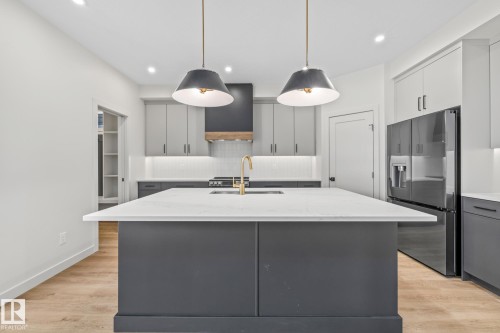 Kitchen featuring gray cabinets, tasteful backsplash, stainless steel fridge with ice dispenser, an island with sink, and hanging light fixtures - 4543 Knight Wynd, Edmonton, AB - Indoor Photo Showing Kitchen With Upgraded Kitchen