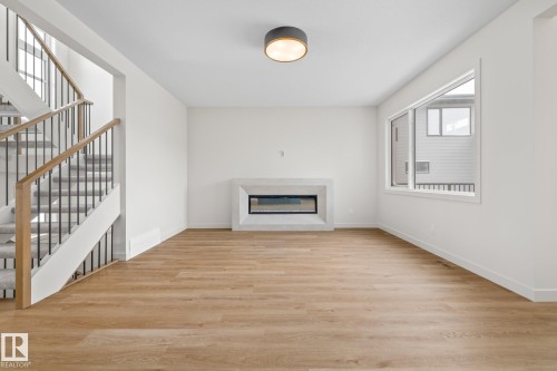Unfurnished living room featuring light wood-type flooring and a glass covered fireplace - 4543 Knight Wynd, Edmonton, AB - Indoor With Fireplace