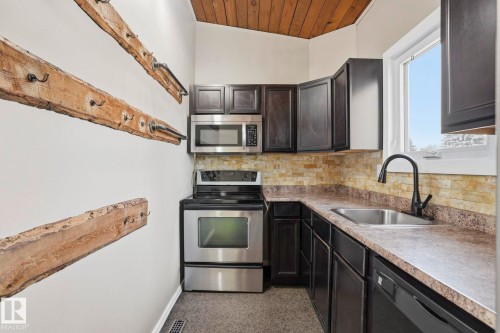 Kitchen with stainless steel appliances, wood ceiling, backsplash, and dark wood finish cabinets - Edmonton, AB - Indoor Photo Showing Kitchen
