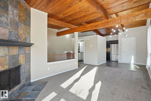 Unfurnished living room featuring wood ceiling, vaulted ceiling with beams, dark carpet, and a fireplace - Edmonton, AB - Indoor