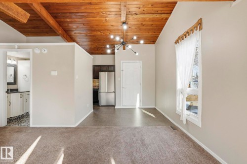 Unfurnished dining area with a wood ceiling with exposed beams, dark colored carpet, and suspended lighting - Edmonton, AB - Indoor Photo Showing Other Room