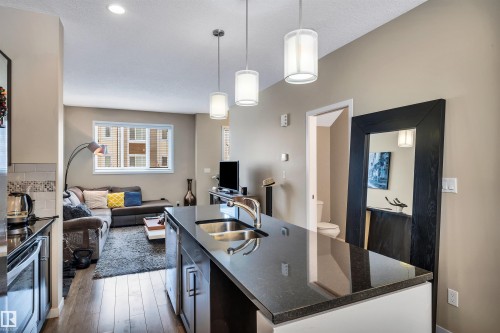 Kitchen featuring a kitchen island with sink, pendant lighting, stainless steel appliances, open floor plan, and dark wood-style flooring - 8 320 Secord Boulevard, Edmonton, AB - Indoor Photo Showing Kitchen With Double Sink With Upgraded Kitchen