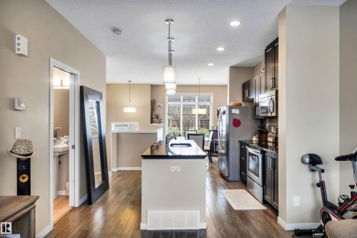 Kitchen with an island with sink, decorative light fixtures, stainless steel appliances, a textured ceiling, and dark wood finished floors - 8 320 Secord Boulevard, Edmonton, AB - Indoor Photo Showing Kitchen