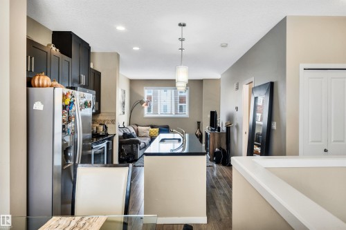 Kitchen with stainless steel appliances, dark wood-style floors, decorative light fixtures, dark cabinetry, and tasteful backsplash - 8 320 Secord Boulevard, Edmonton, AB - Indoor