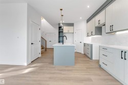 Kitchen with hanging light fixtures, a center island with sink, light wood finished floors, light stone counters, and gray cabinets - 