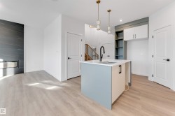 Kitchen featuring open shelves, hanging light fixtures, light wood-style floors, and a center island with sink - 